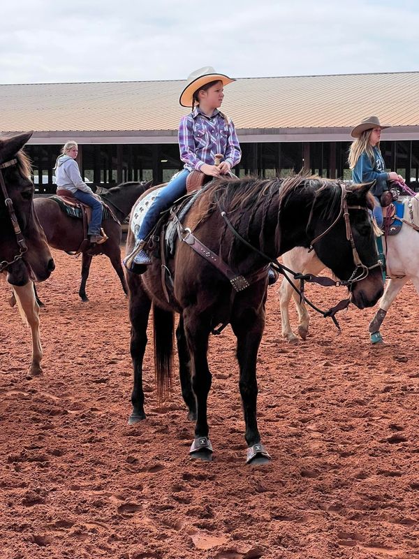 Adeline in a cowboy hat on Boots in a dirt arena, ready to run